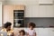 La imagen muestra a un padre joven con sus dos hijas en una cocina, con la unidad interior de un sistema de aire acondicionado Carrier en la pared.
