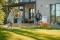 Una familia disfruta de su jardín frente a una casa moderna con una aerotermia aire-agua instalada en la pared.
